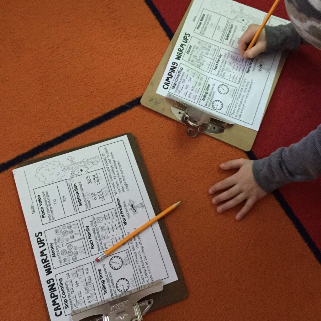 Students completing Camp Read a Lot math warm-ups on clipboards during camping theme day