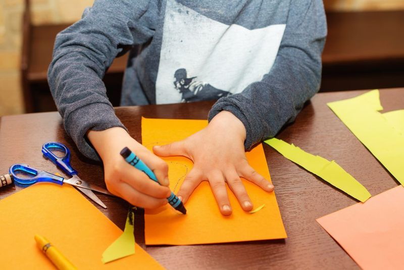 Fun fine motor activities for kids – child tracing hand on orange paper with crayon to build pencil grip, scissor skills, and coordination.