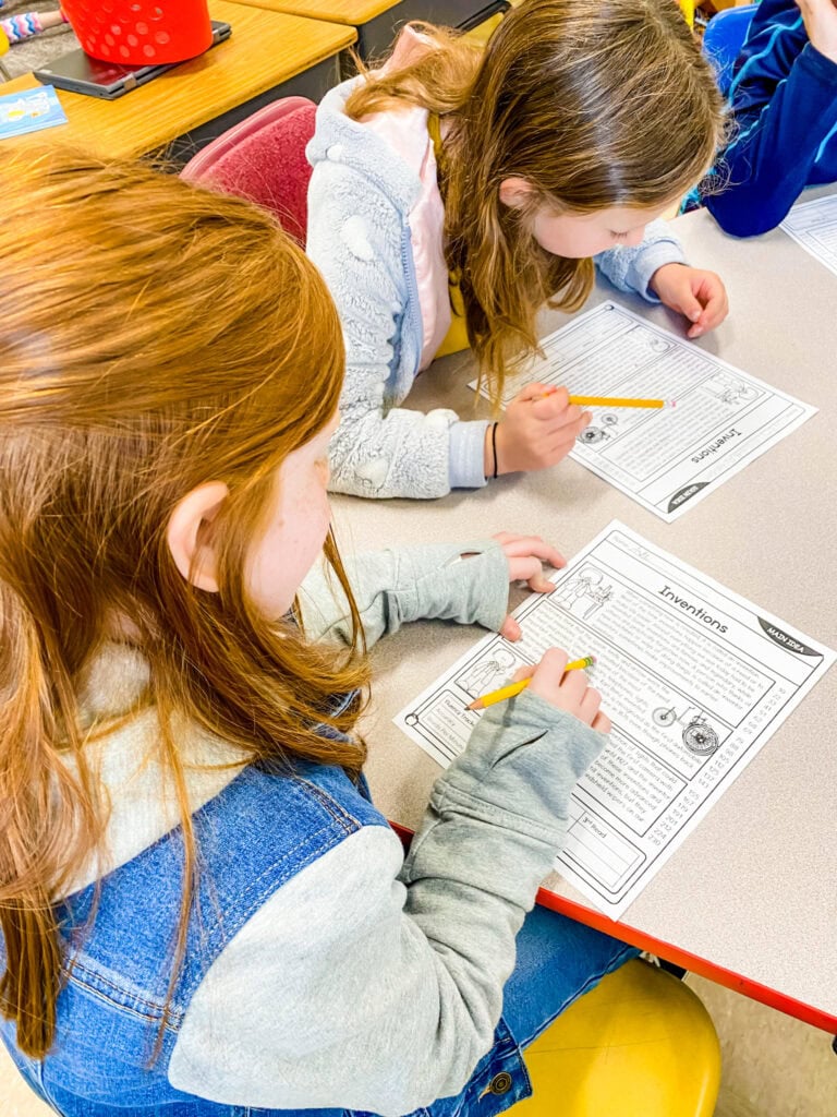 Image showing students working together on reading worksheets at a table as part of structured buddy reading activities in the classroom.